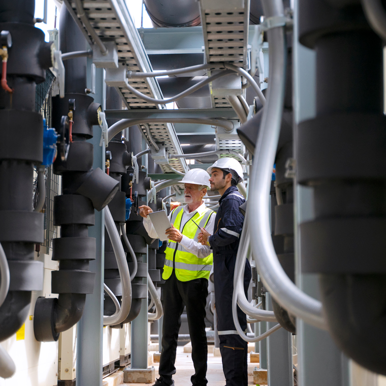 Two men inspecting black foam insulation installed pipe systems